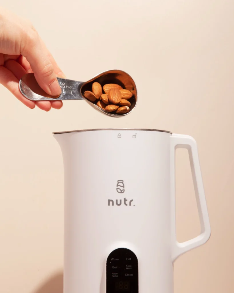 Hand adding almonds to a Nutr plant-based milk maker machine